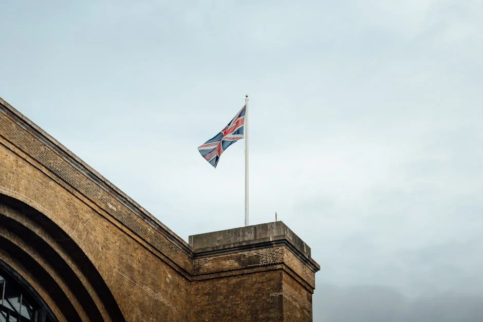 Union Jack flag waving atop a historic brick building in London, UK, against a cloudy sky. - iptv uk