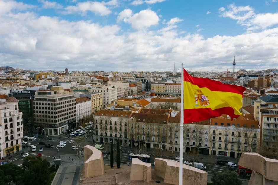 Drone view of Spanish city with aged buildings and national flag under cloudy blue sky - iptv espaa