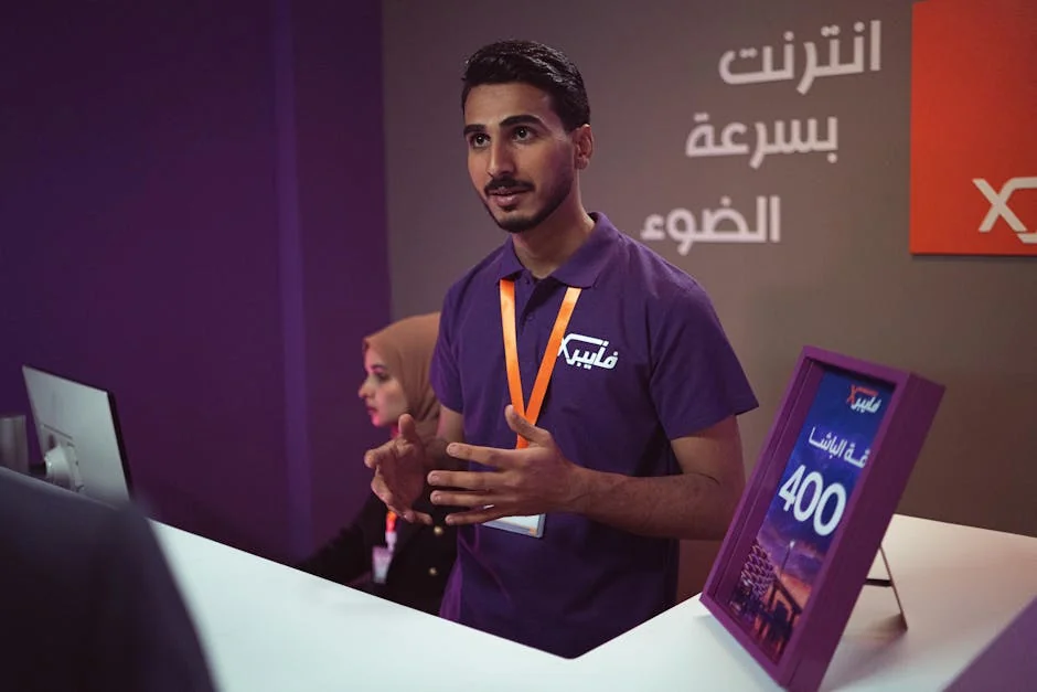 Man at a tech booth explaining features to a customer indoors with promotional banner. - iptv service