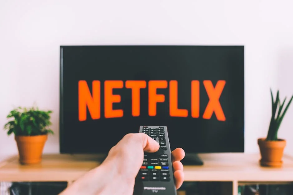 A hand holding a TV remote in front of a screen with Netflix, perfect for streaming and movie night themes. - iptv subscriptions